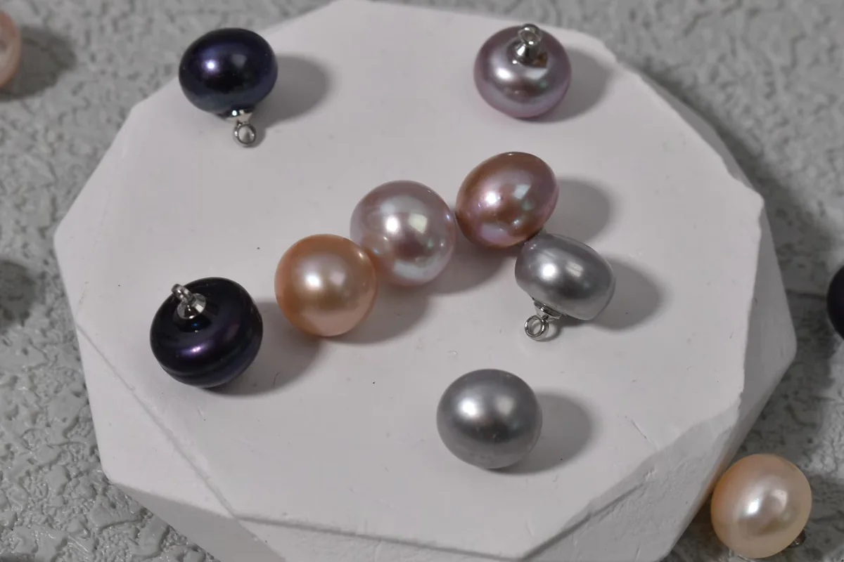 Pearls in peach, gray and dark tones, some fitted with metal loops, on a round white display.
