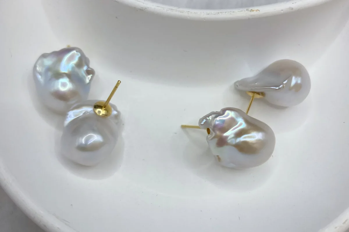 Four irregular white pearl stud earrings with gold-colored posts on a white dish.