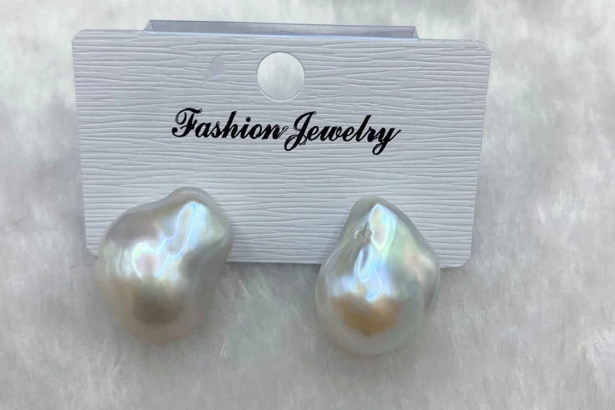 Large white baroque pearl studs on a textured display card.