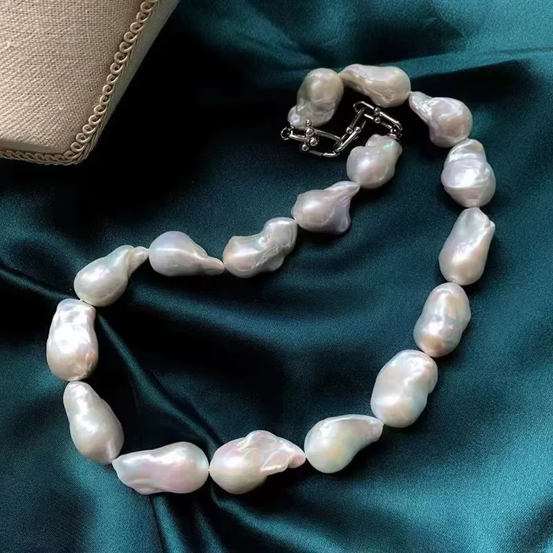 A white baroque pearl necklace resting on dark teal satin.