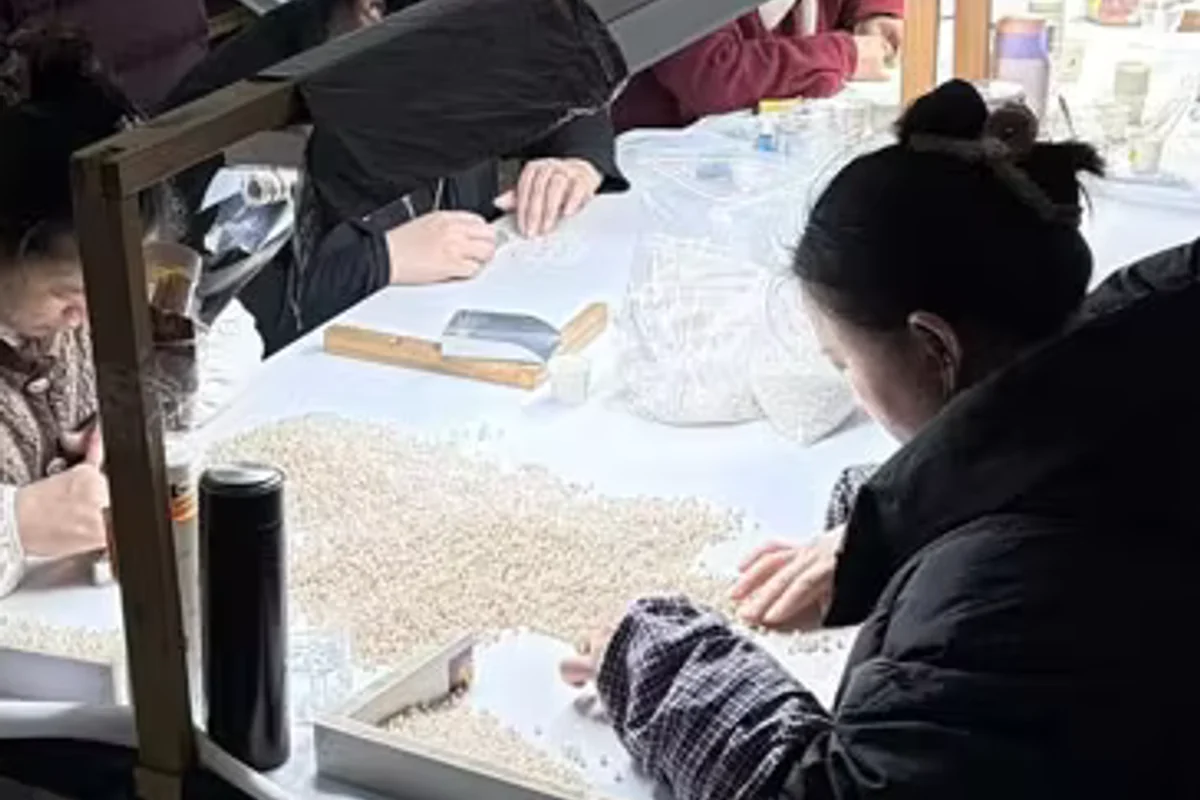 Workers examining white pearls under task lights.