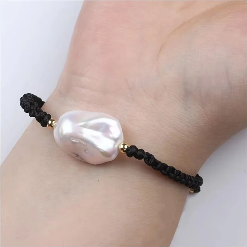 A black braided bracelet with a large white baroque pearl worn on a wrist.