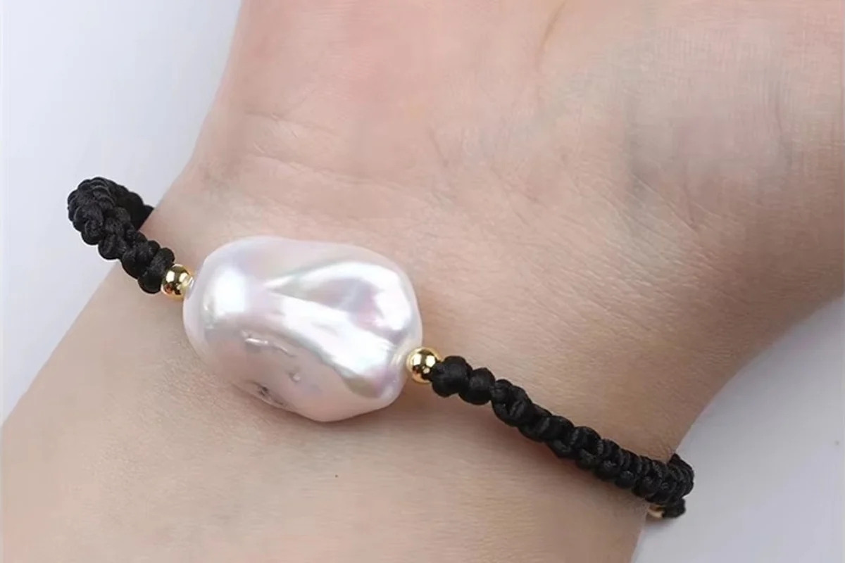 A braided cord and baroque pearl bracelet shown on a wrist.