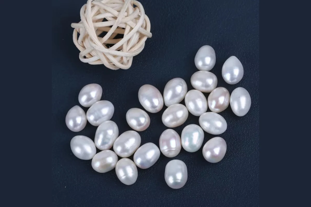 Loose white drop and oval pearls on a dark blue surface.