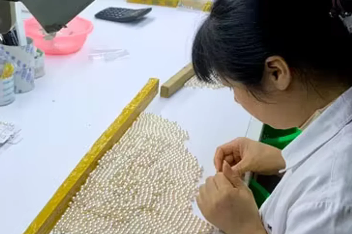 A worker selecting rows of white pearls at a worktable.