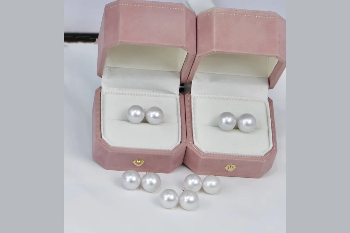 White pearl studs in open blush pink jewelry boxes.