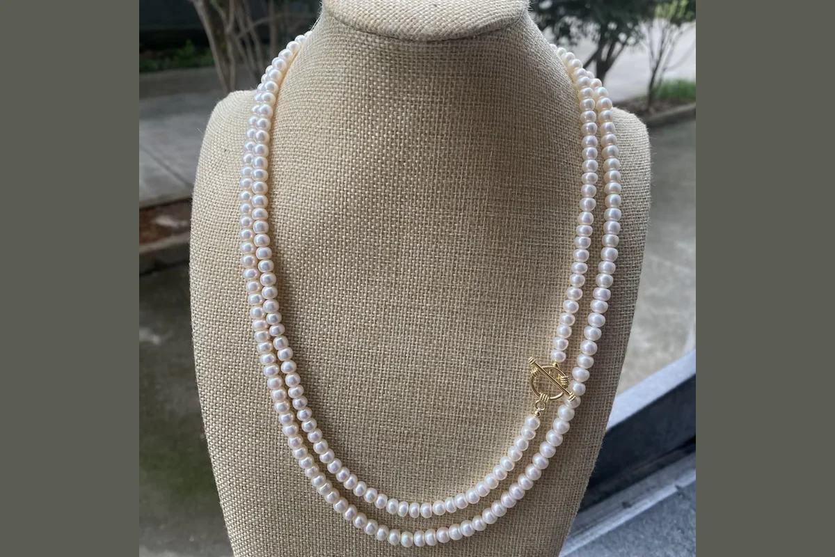 Long white pearl necklace wrapped in two lengths on a linen jewelry bust
