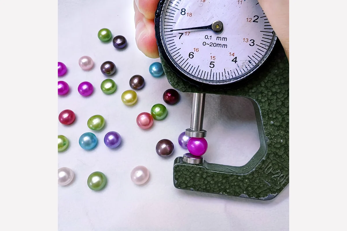 A dial gauge measuring a colored pearl beside loose pearls