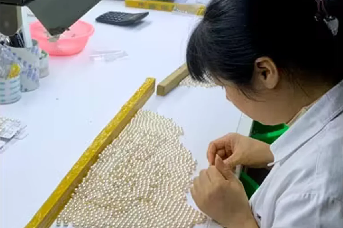 A worker matching rows of white pearls at a worktable