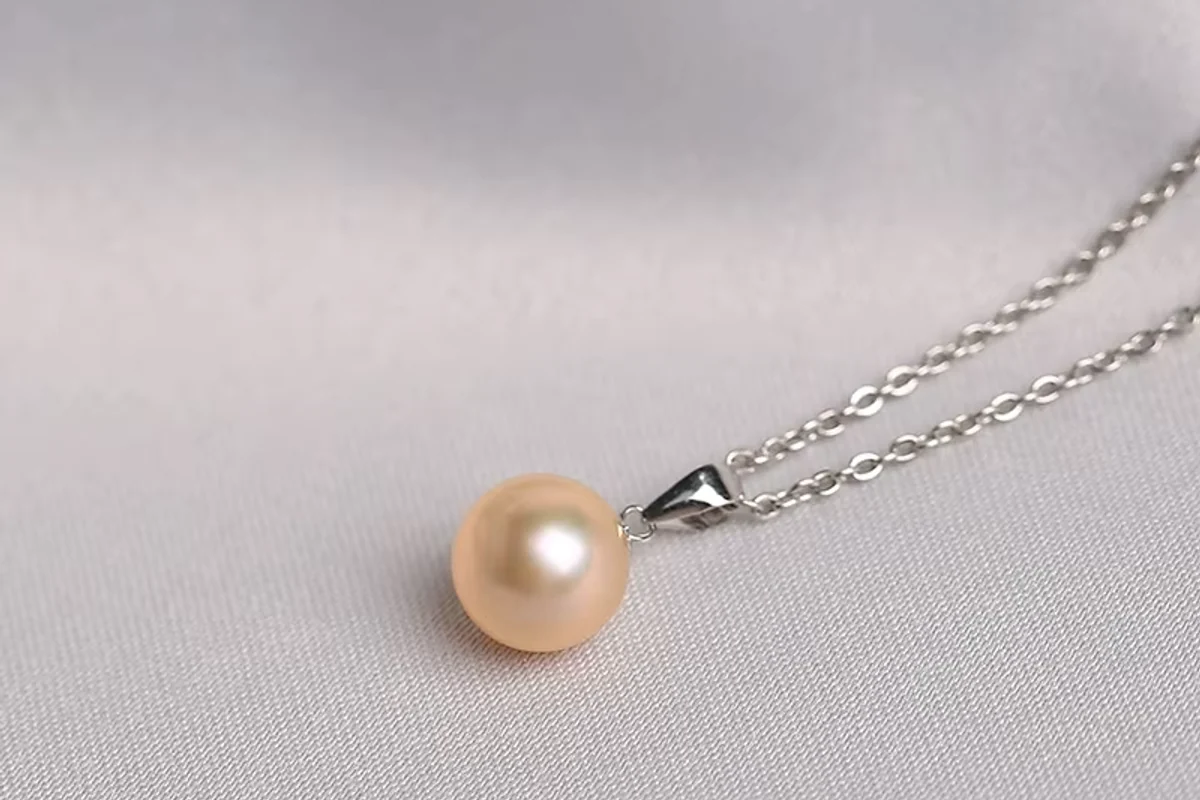 Peach pearl pendant and chain resting on pale fabric