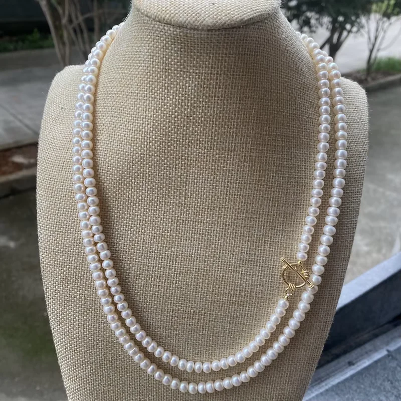A long white pearl necklace arranged in two lengths on a linen bust.