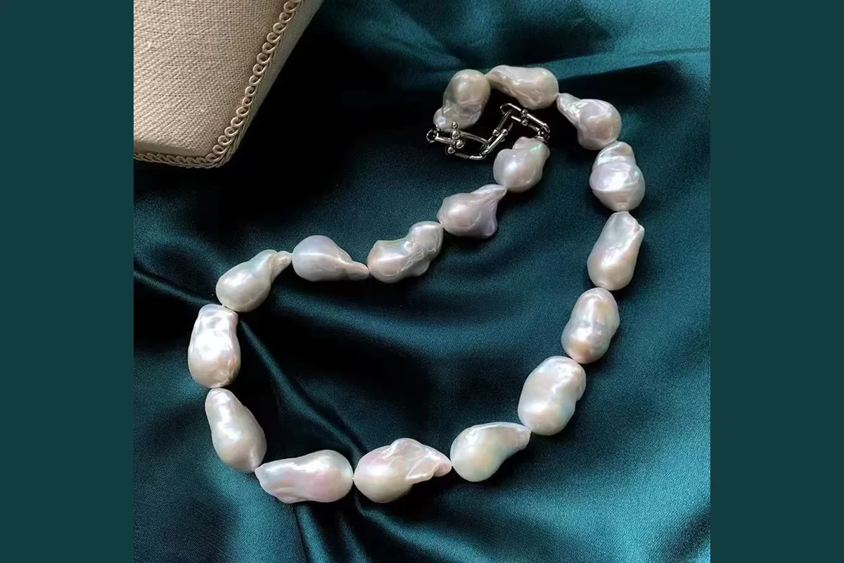 Irregular white pearl necklace arranged on dark teal satin