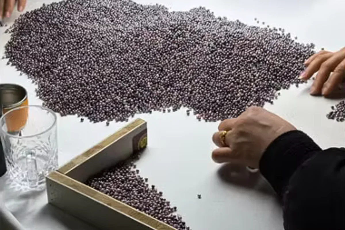 Hands sorting dark pearls across a white worktable