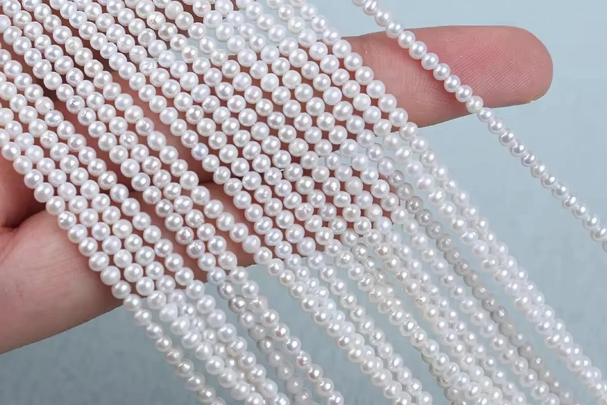 Hand holding several strands of small white pearls
